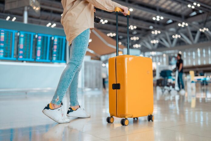 Young,Female,Traveler,Passenger,Walking,With,A,Yellow,Suitcase,At